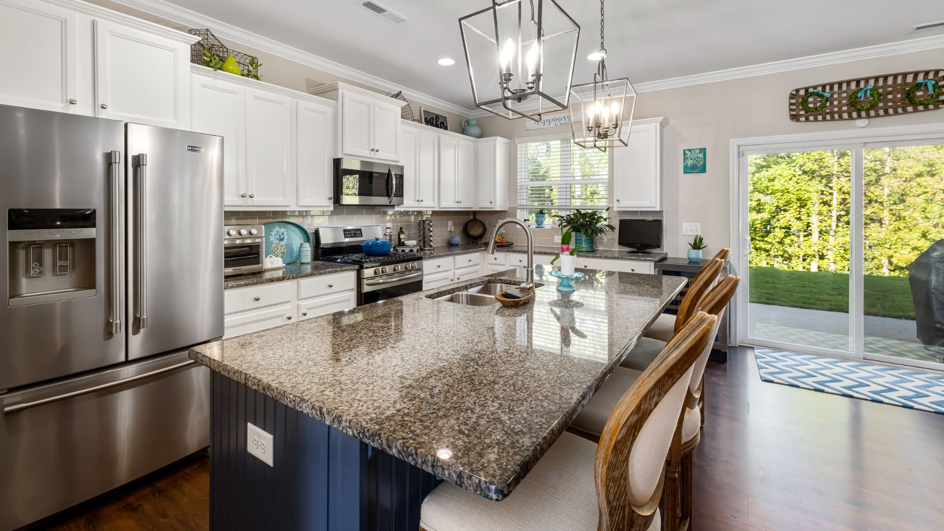 Modern white kitchen with granite island, stainless steel appliances, and garden view