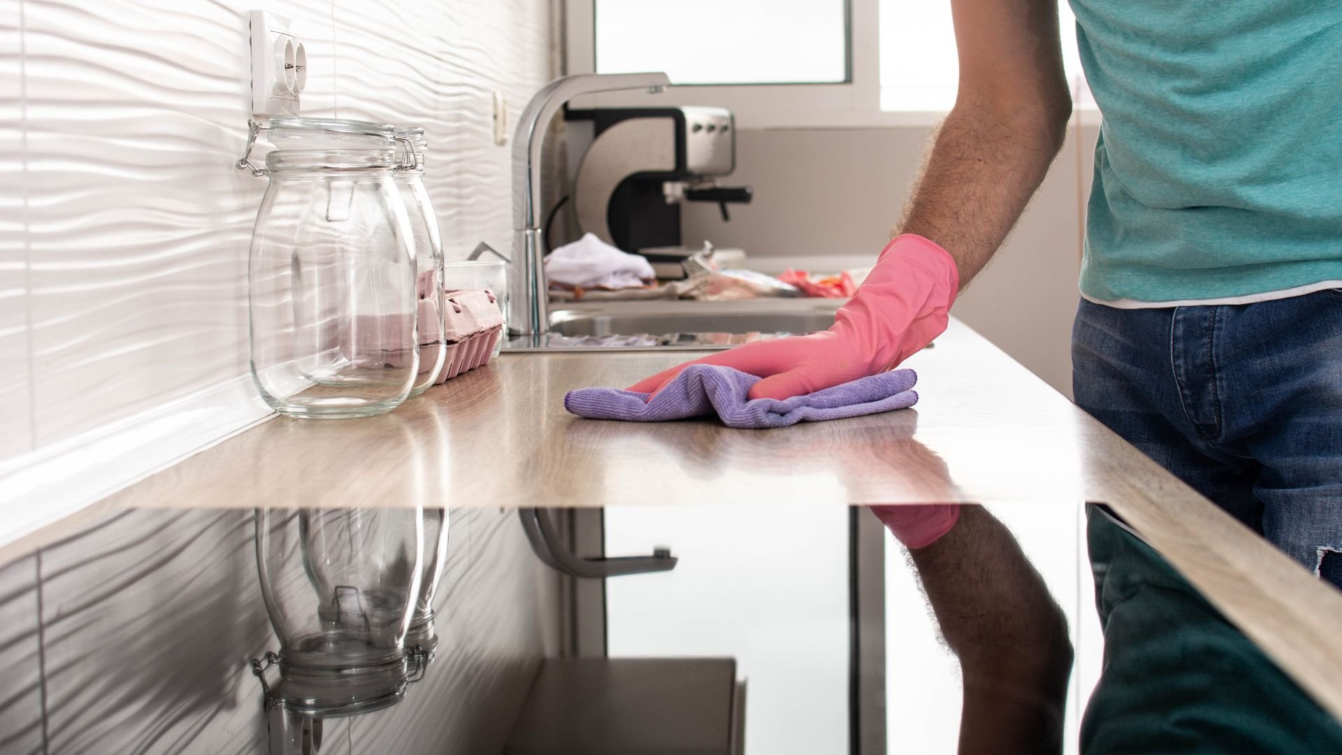 Person cleaning kitchen counter with pink gloves and purple cloth