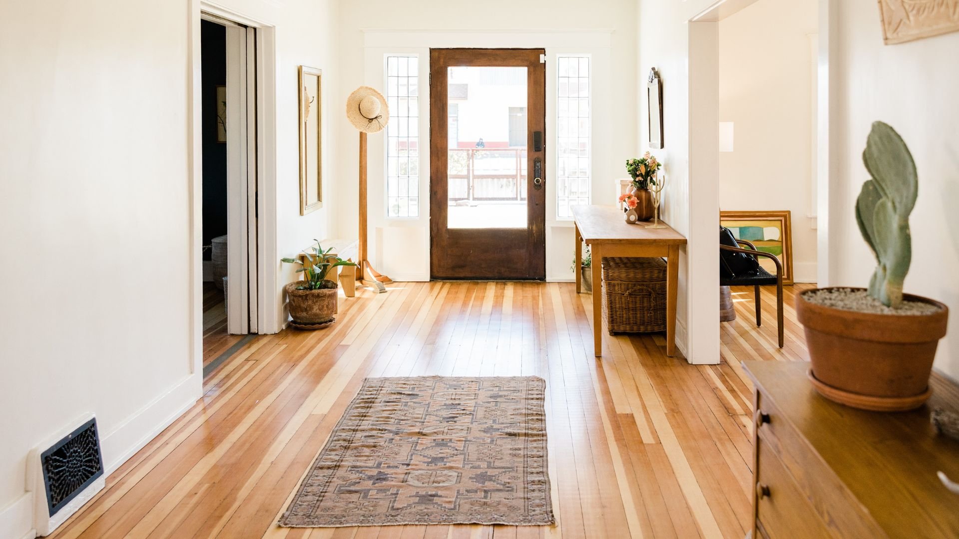 Bright entryway with wooden floor, plants, straw hat, and glass door