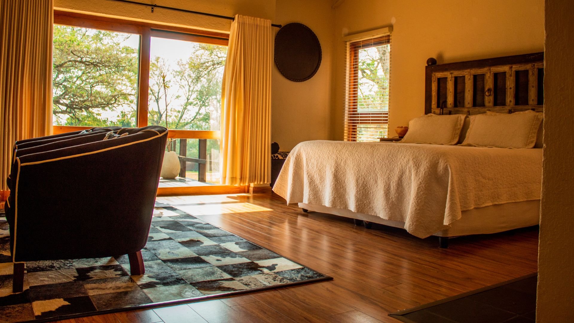 Cozy bedroom with wooden floor, armchair, and large windows overlooking trees