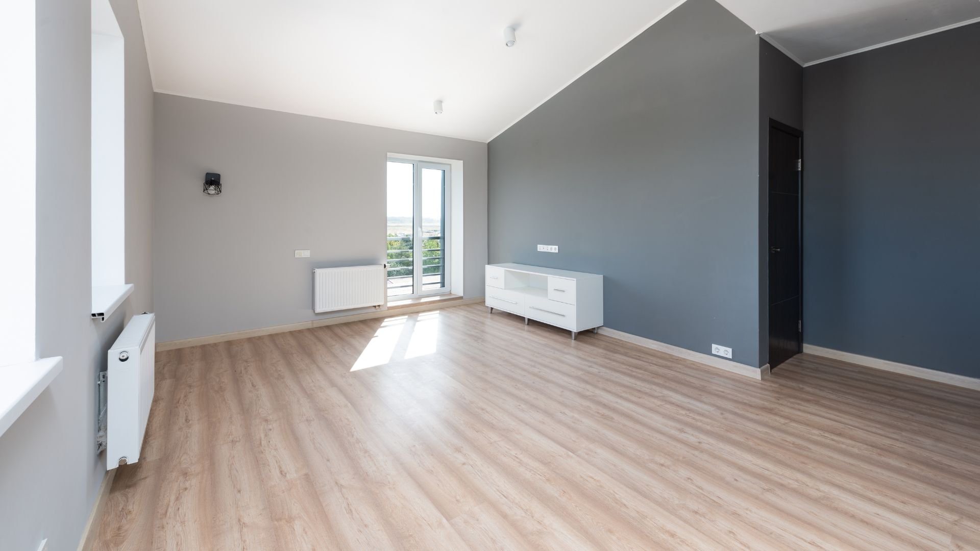 Empty room with wooden floor, gray walls, white cabinet, and balcony door