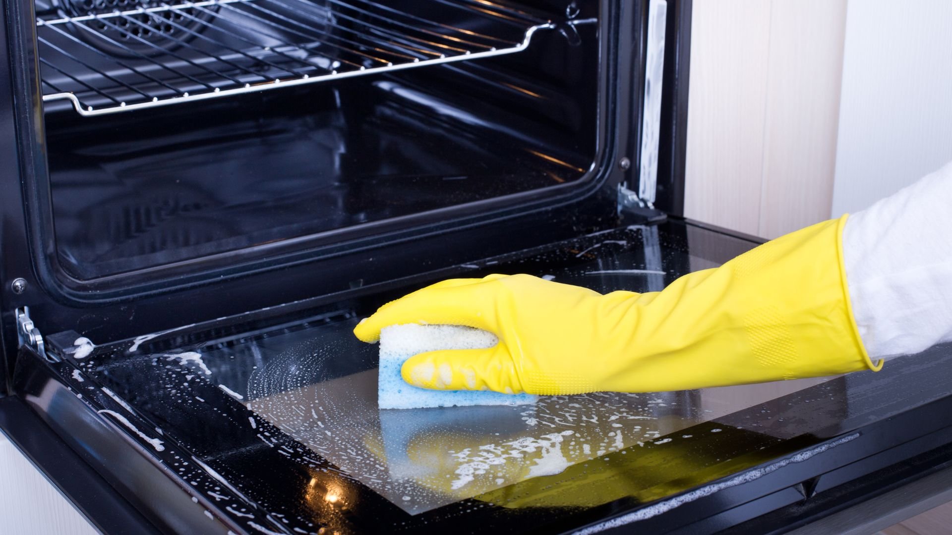 Yellow gloved hand cleaning inside of oven with sponge